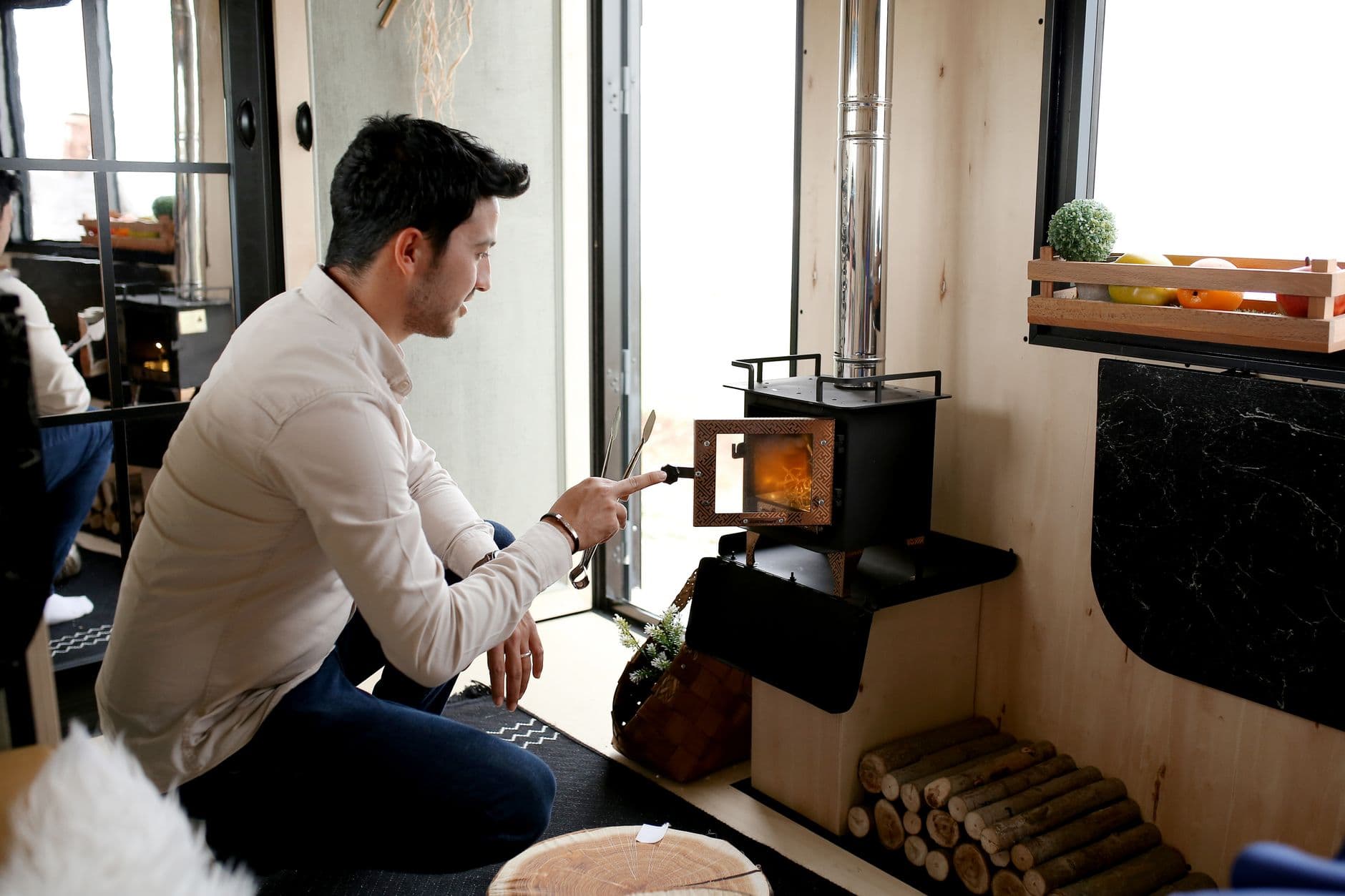 A man lights a wood stove inside a cozy room, creating a warm and inviting atmosphere.